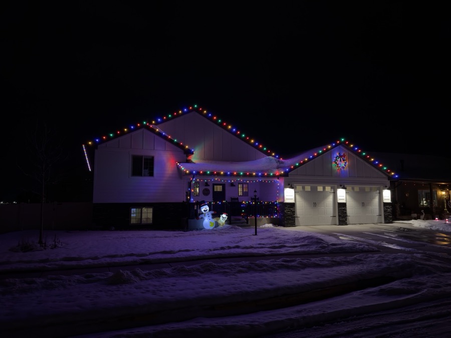 Two-story home with multicolor roofline lights, a lit wreath and snow on the ground